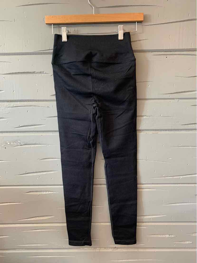 Black high-waist slim-fit pants with subtle ribbed texture hanging on wooden hanger.