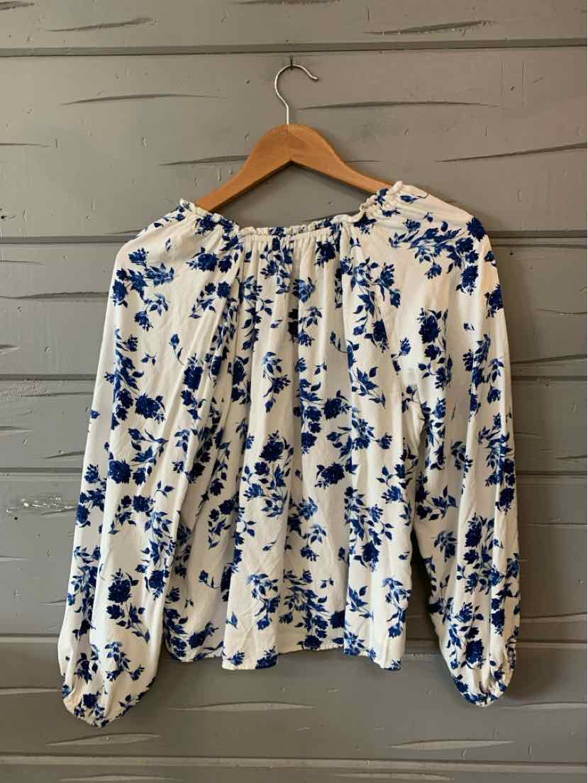 White long-sleeve blouse with blue floral print, round neckline, and gathered cuffs.