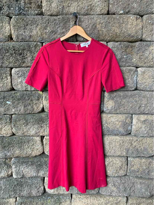 Pink short-sleeve knee-length dress with round neckline hanging on wooden hanger against stone wall.