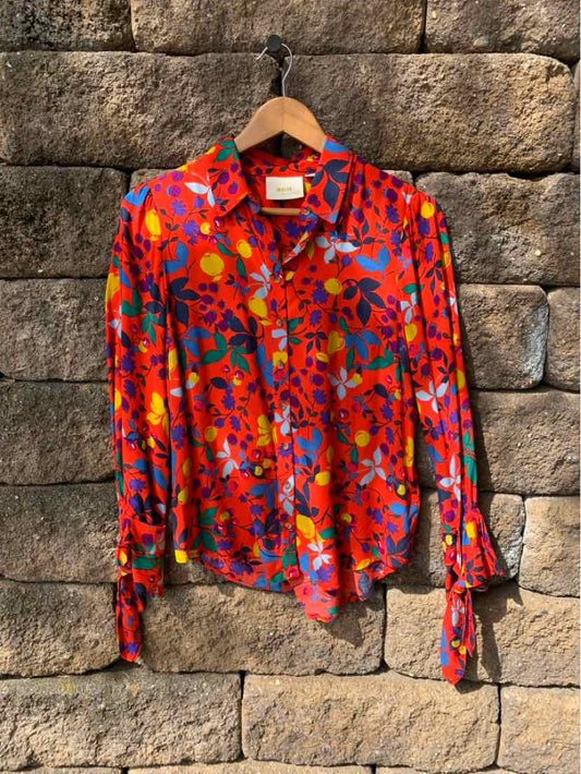 Long-sleeve red blouse with vibrant floral print and buttoned cuffs hanging on wooden hanger.