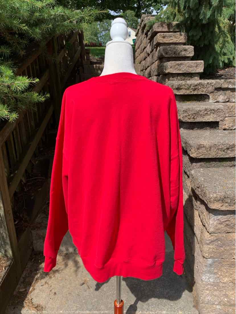 Bright red oversized sweatshirt with long sleeves and ribbed cuffs on a mannequin outdoors.