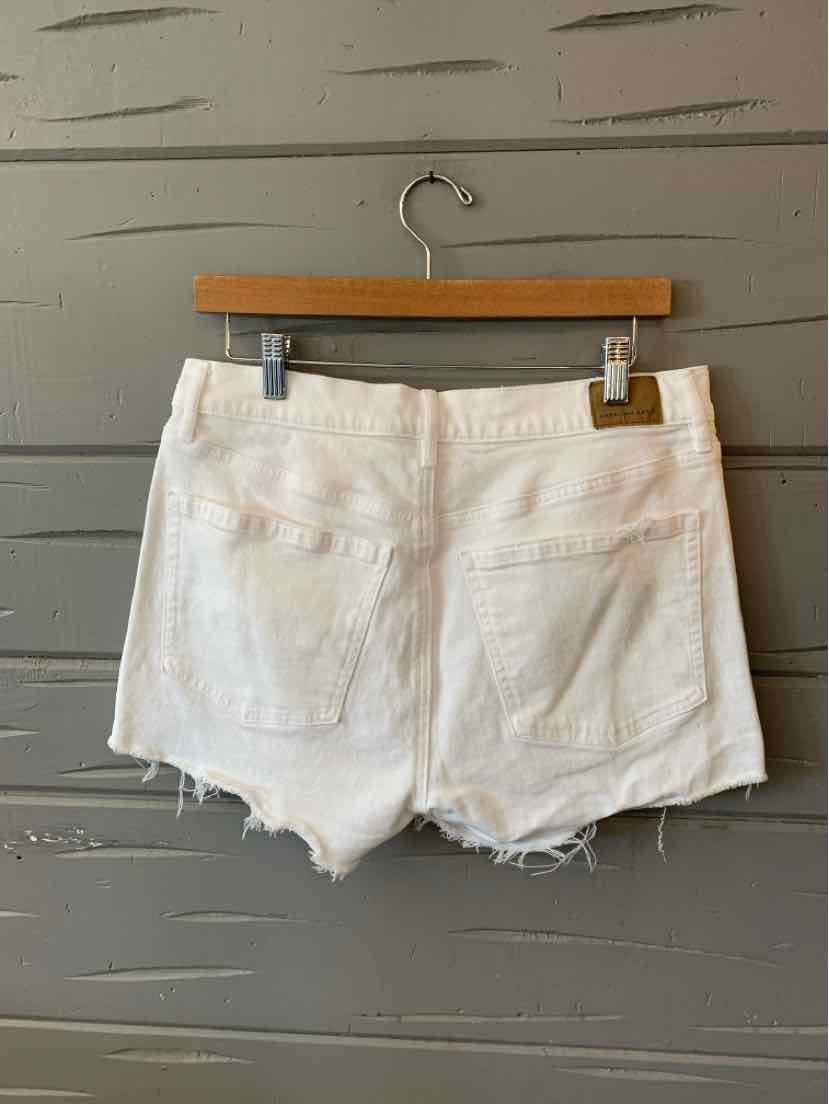 White denim shorts with frayed hems, five-pocket design, and belt loops hanging on wooden hanger.