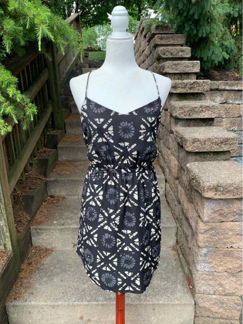 Black sleeveless dress with white geometric floral pattern and adjustable thin straps.