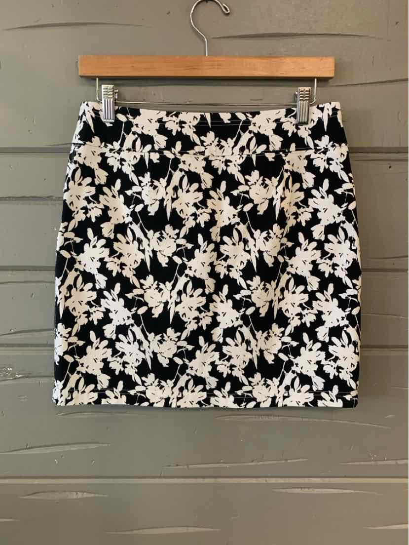 Black mini skirt with white floral print and front zipper detail on wooden hanger.