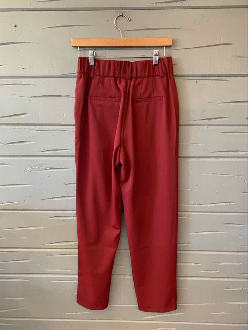 Solid burgundy-red pants with a gathered elastic waistband and straight, relaxed legs, hanging on a wooden hanger.