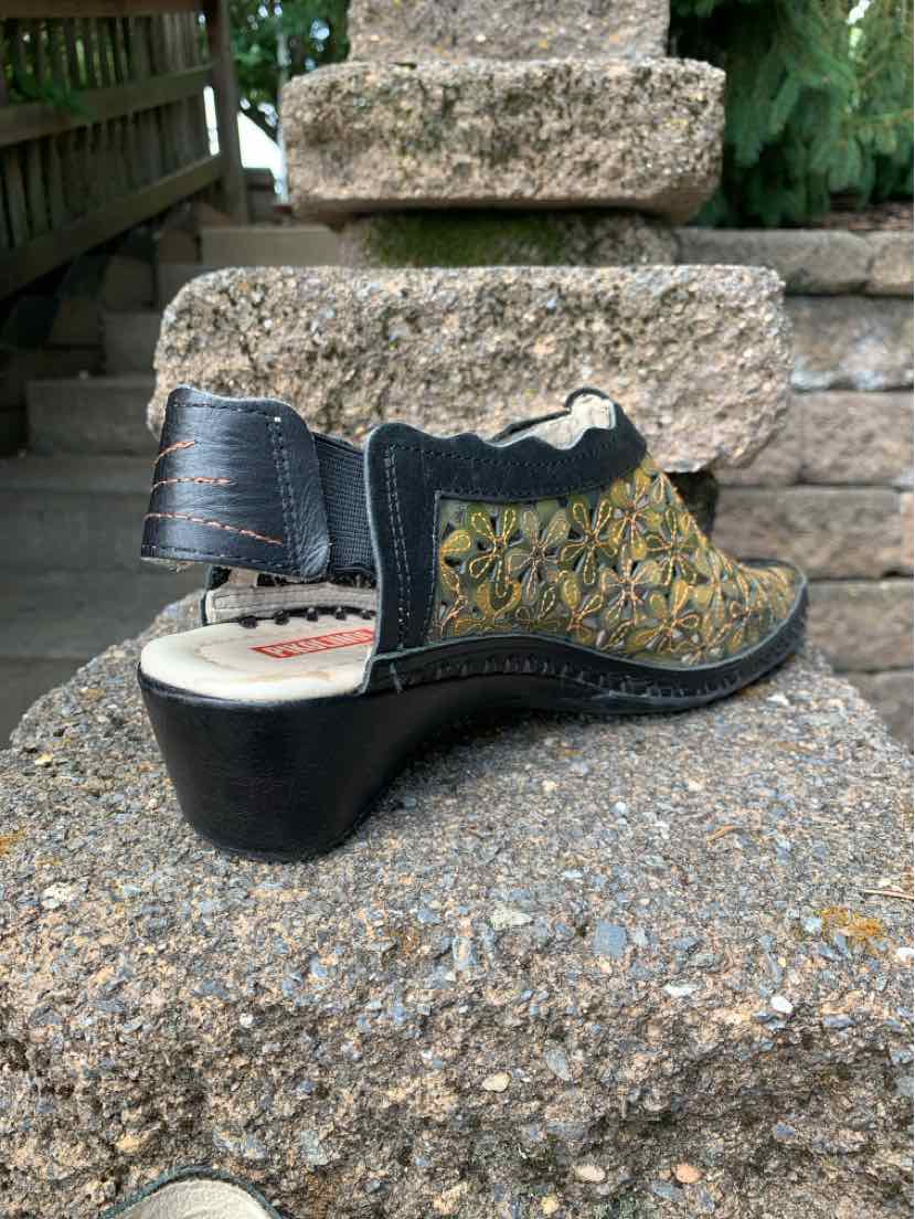 Black leather wedge sandal with floral cutout design, ankle strap, and open heel.