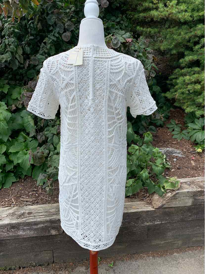 White short-sleeve lace dress with intricate floral pattern and back zipper closure on mannequin outdoors.