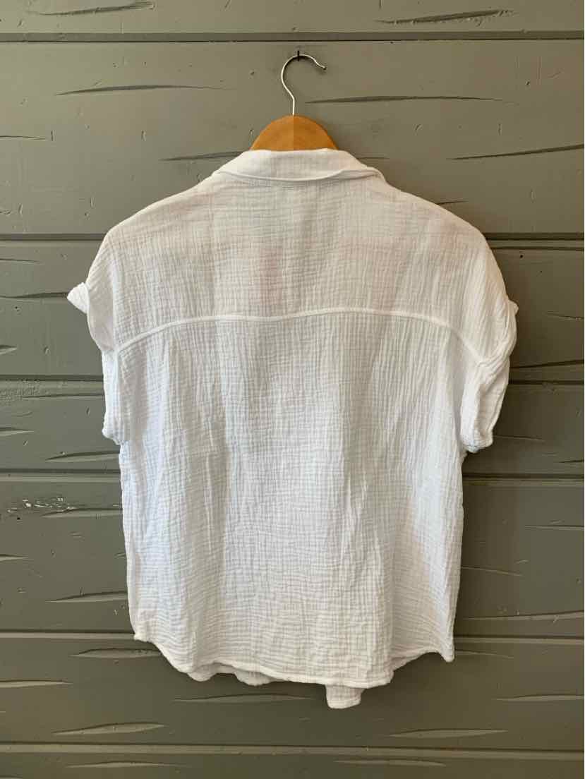 White textured short-sleeve blouse with rolled cuffs and a relaxed fit hanging on wooden hanger.