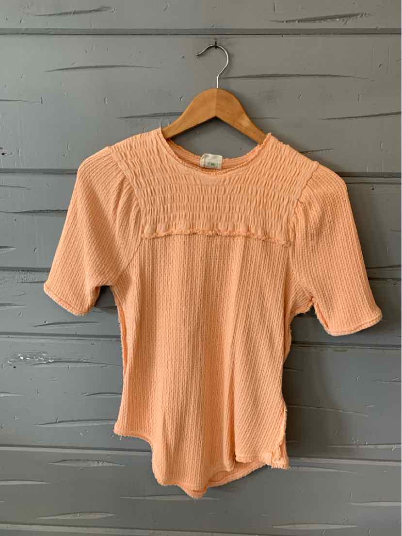 Light orange ribbed short-sleeve top with textured yoke detail and round neckline on wooden hanger.