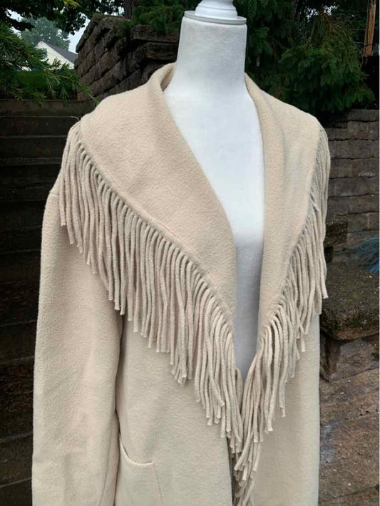 Tan oversized cardigan with long fringe trim along the open front and pockets, soft knit fabric.