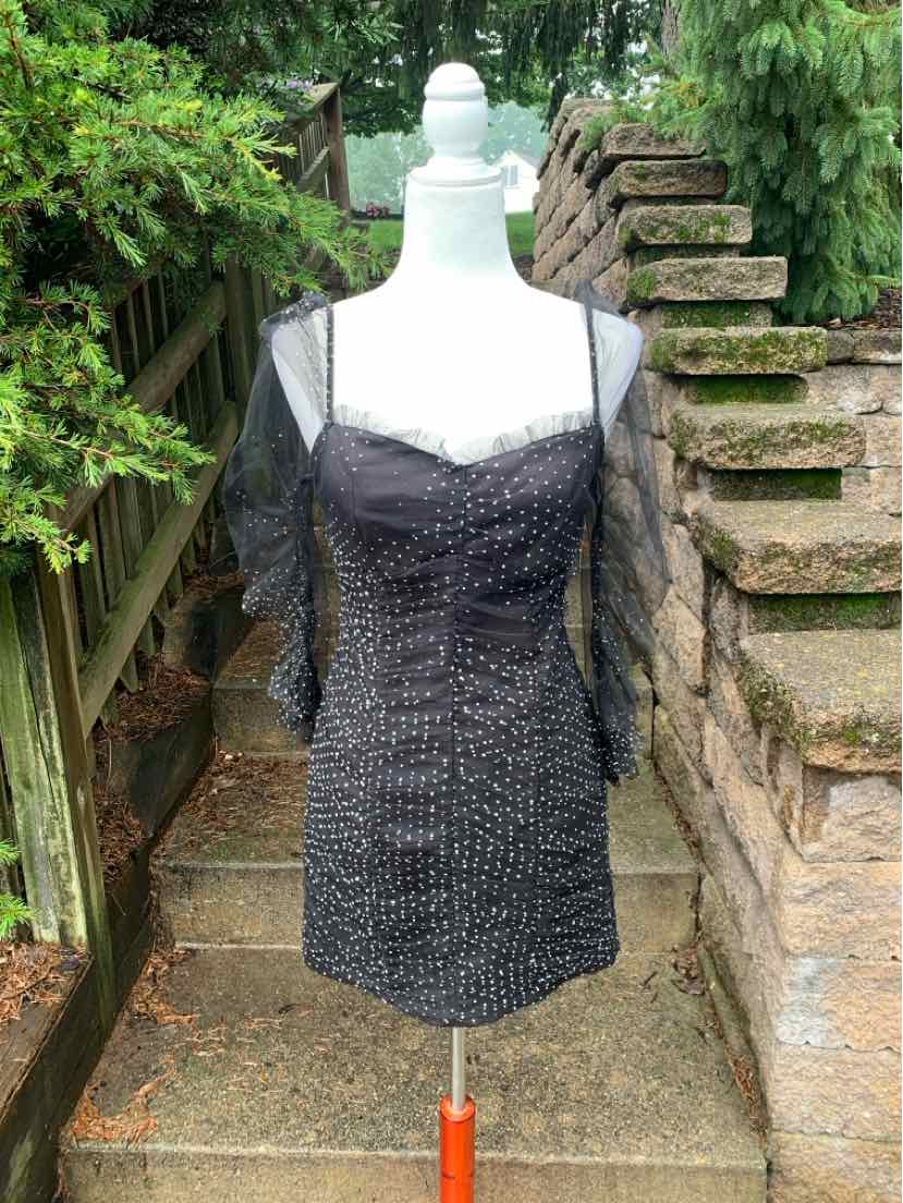 Black mini dress with sheer polka dot sleeves and ruched bodice on white mannequin outdoors.