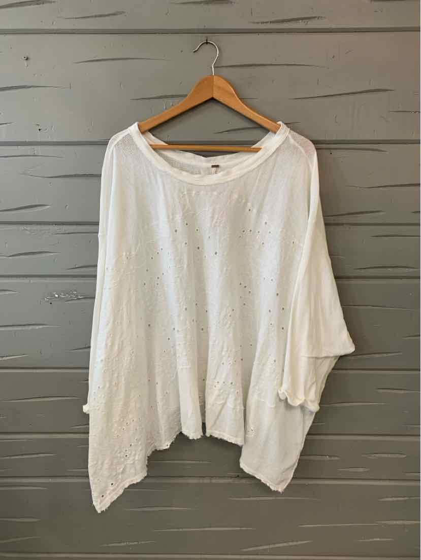 White oversized cotton knit top with wide neckline and asymmetrical hem on wooden hanger.
