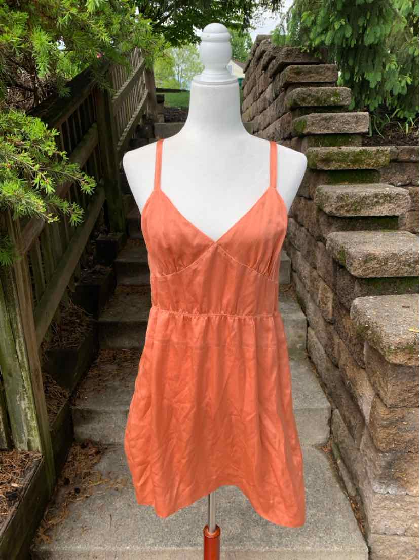 Sleeveless orange silk mini dress with thin straps and gathered waist on white mannequin outdoors.