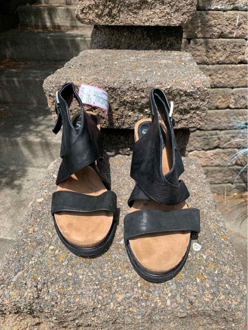 Black leather open-toe sandals with adjustable back straps and tan cushioned footbeds.