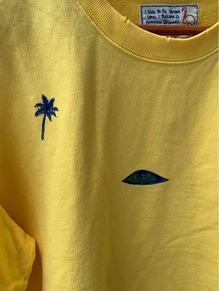 Yellow short-sleeve t-shirt with small embroidered navy palm tree and green hill details on front.