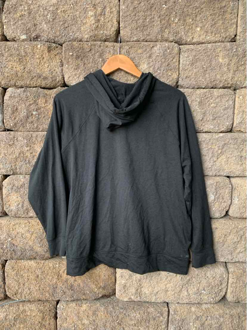 Charcoal gray lightweight hoodie with long sleeves and relaxed fit hanging on wooden hanger against stone wall.