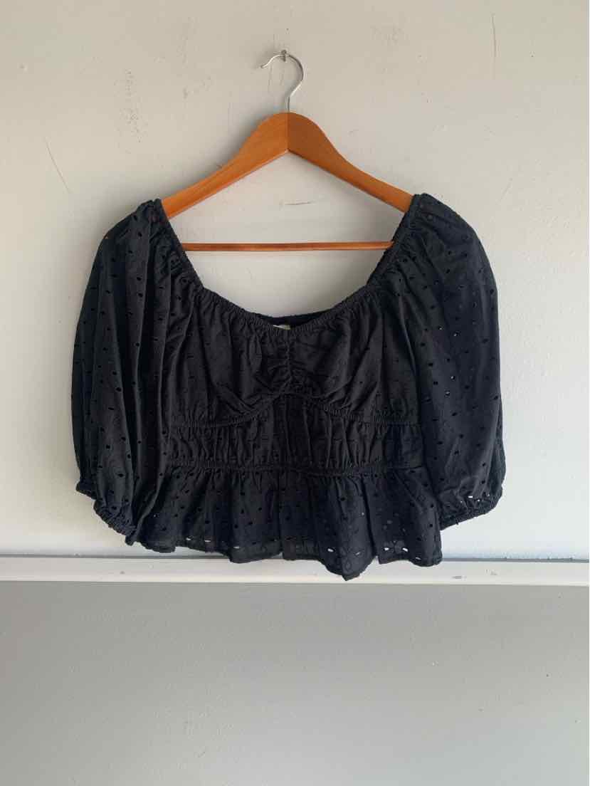 Black eyelet fabric crop top with puff sleeves and scoop neckline on wooden hanger.