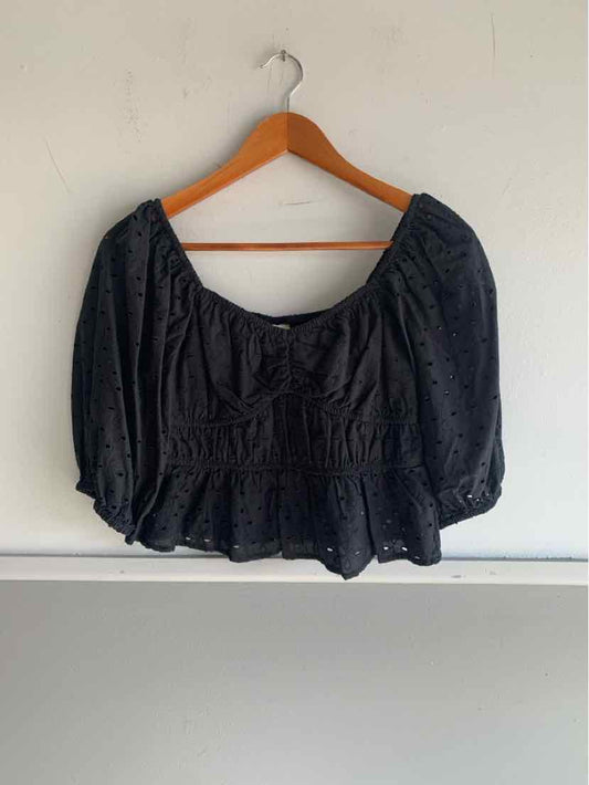 Black eyelet fabric crop top with puff sleeves and scoop neckline on wooden hanger.