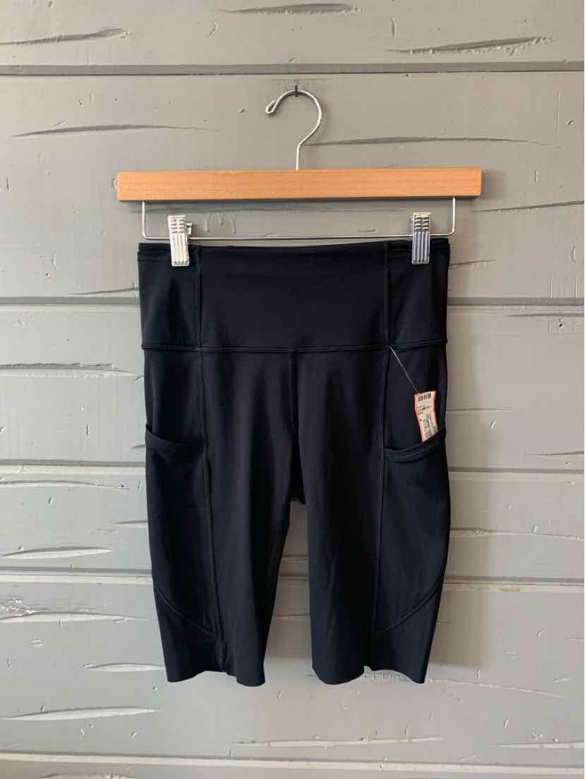 Black high-waisted athletic shorts with side pockets, knee-length, stretchy fabric.