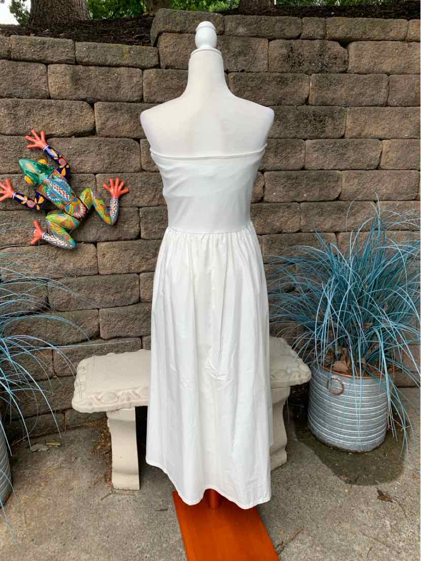 White sleeveless midi dress with gathered waist and smooth fabric, styled on a mannequin outdoors.