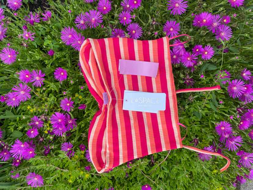 Pink and red striped sleeveless crop top with thin straps laid on purple flowers.