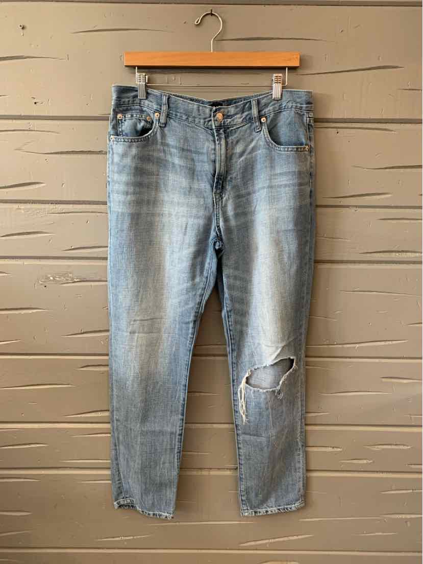 Light blue denim jeans with distressed knee and frayed hems hanging on wooden hanger.