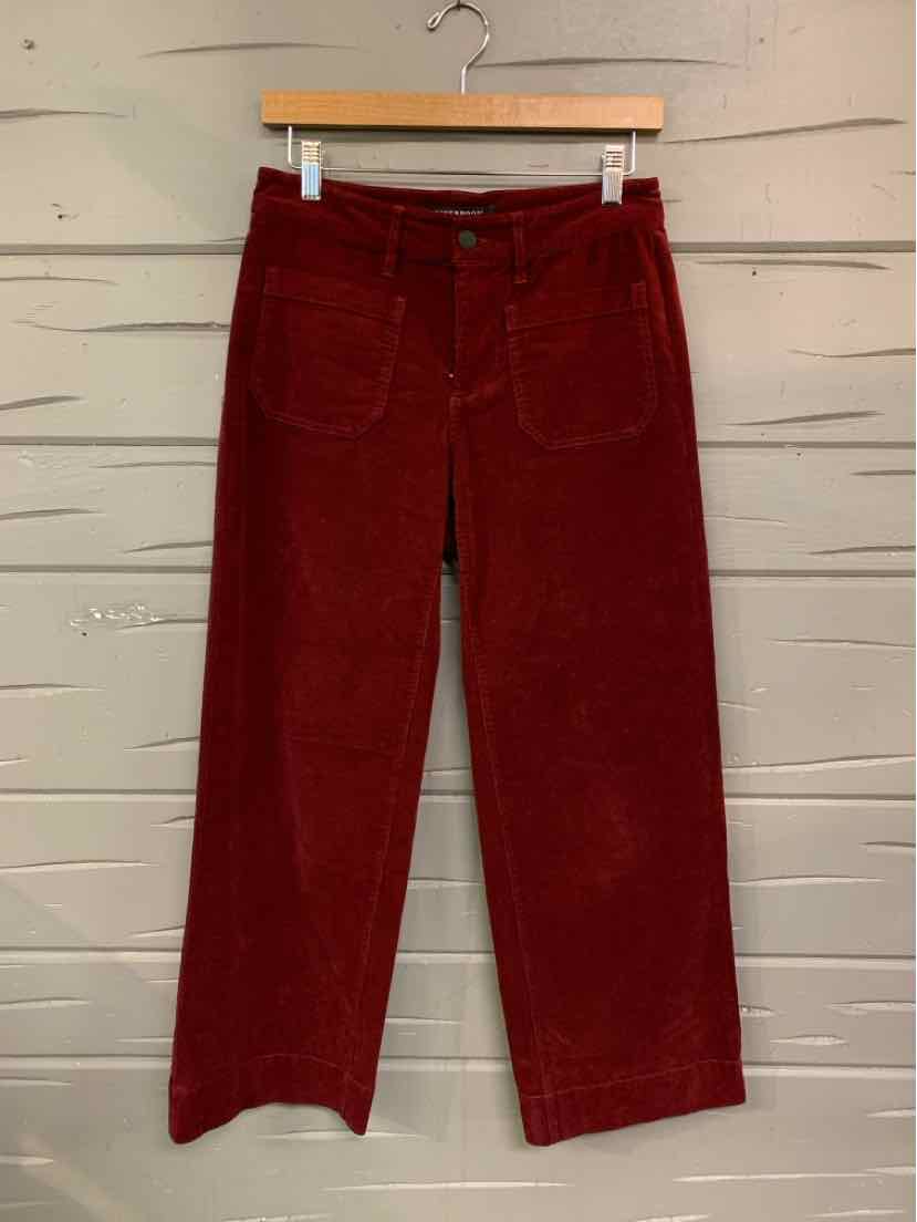 High-waisted burgundy corduroy pants with front patch pockets and wide legs hanging on wooden hanger.