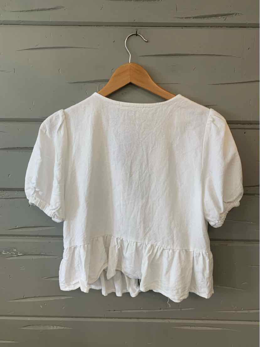 White short-sleeve blouse with ruffled hem and gathered sleeves on wooden hanger.
