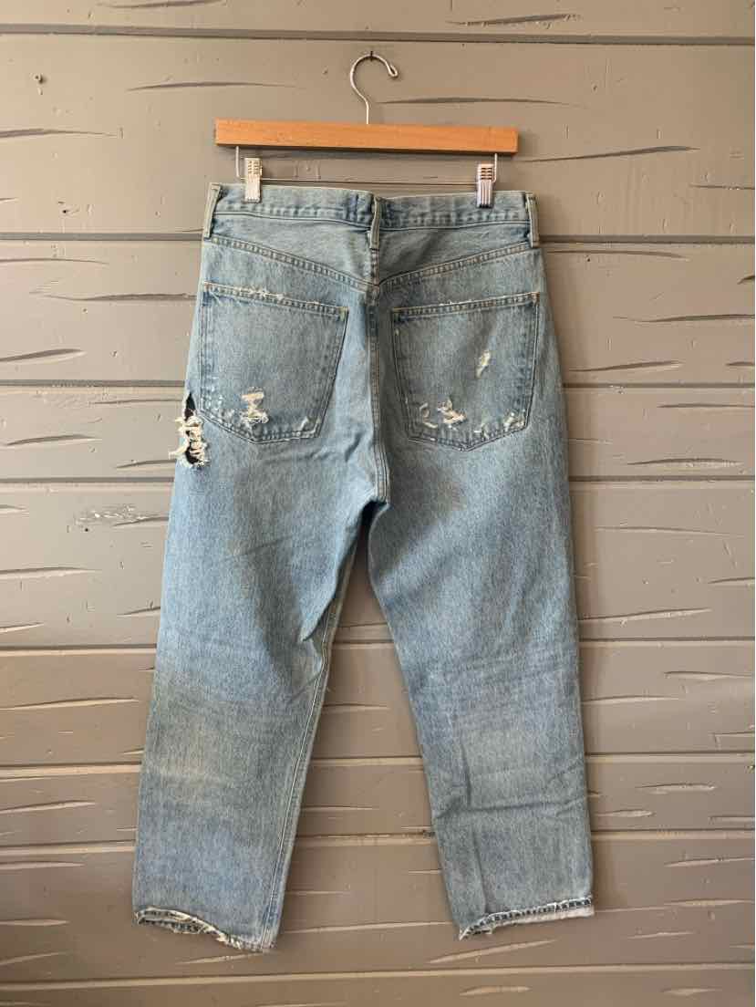 Light blue distressed denim jeans with frayed hems and back pockets hanging on wooden hanger.