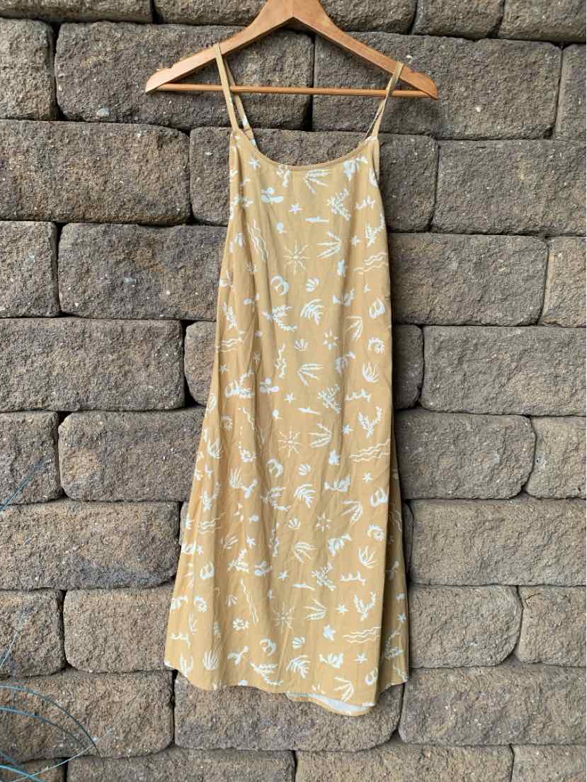 Tan sleeveless midi dress with white floral print and thin straps hanging on wooden hanger.