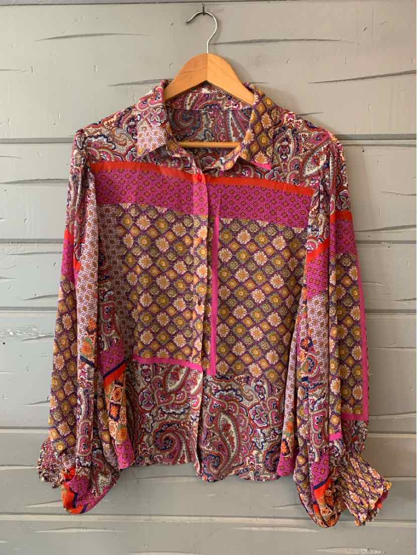Long-sleeve blouse with vibrant multi-pattern combining paisley and geometric prints in red, pink, purple, and gold tones.