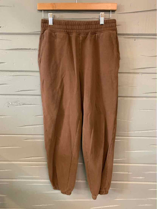 Brown solid jogger pants with elastic waistband and gathered cuffs hanging on wooden hanger.